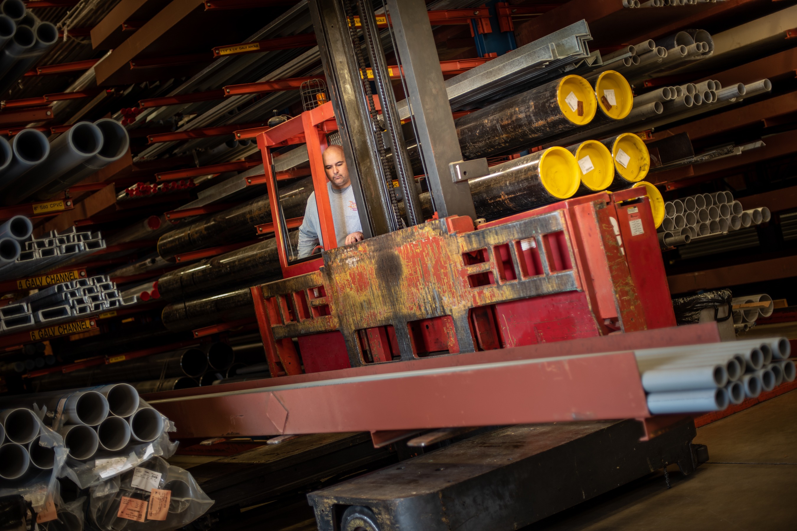 man on forklift moving pipes in warehouse